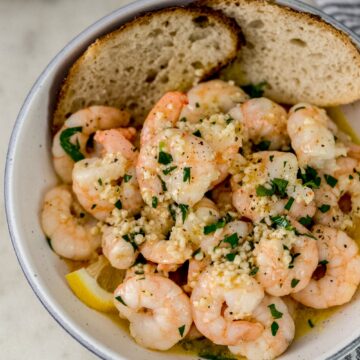 overhead view garlic butter shrimp in white serving bowl with bread and lemon wedges