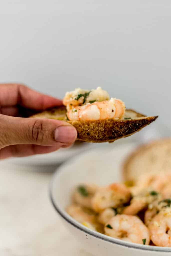 hand holding piece of bread with shrimp on it. 