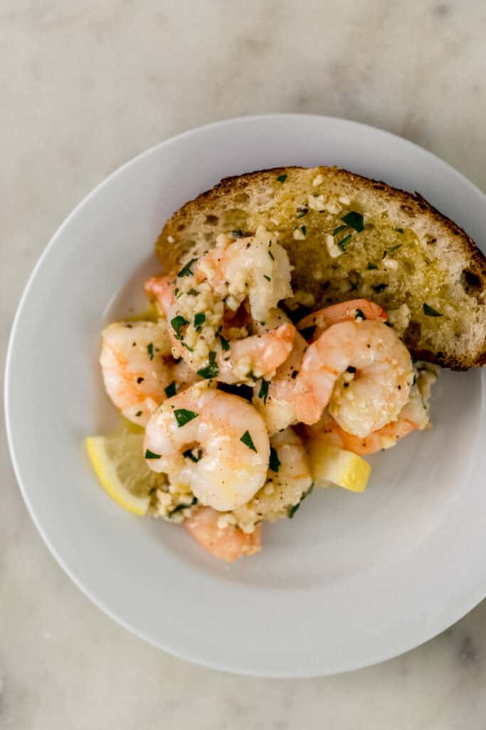 white plate with garlic butter shrimp, lemon, and bread on it. 