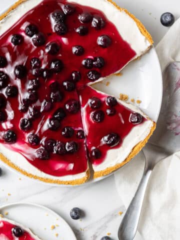 overhead view of blueberry cheesecake with a piece cut out of it on a white plate.