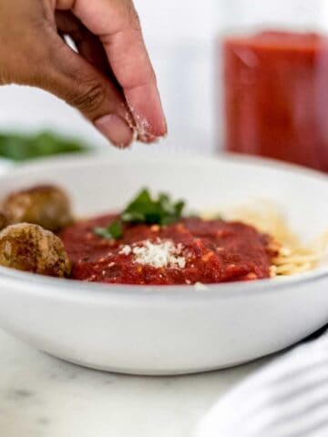 hand sprinkling cheese over bowl of pasta