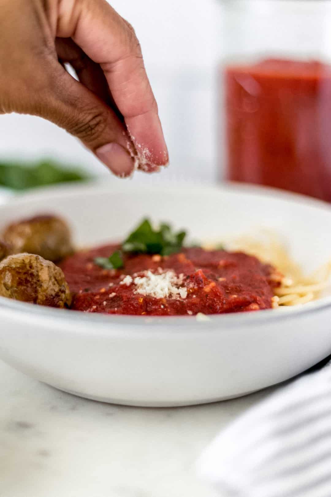 hand sprinkling cheese over bowl of pasta