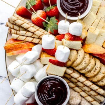 Overhead view of dessert board with chocolate fondue dippers on it on marble surface.