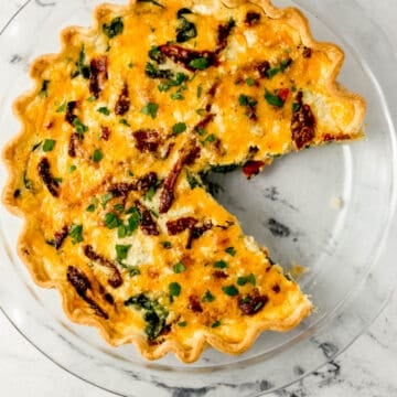 overhead view of baked quiche in a glass pie pan with a piece cut out of it