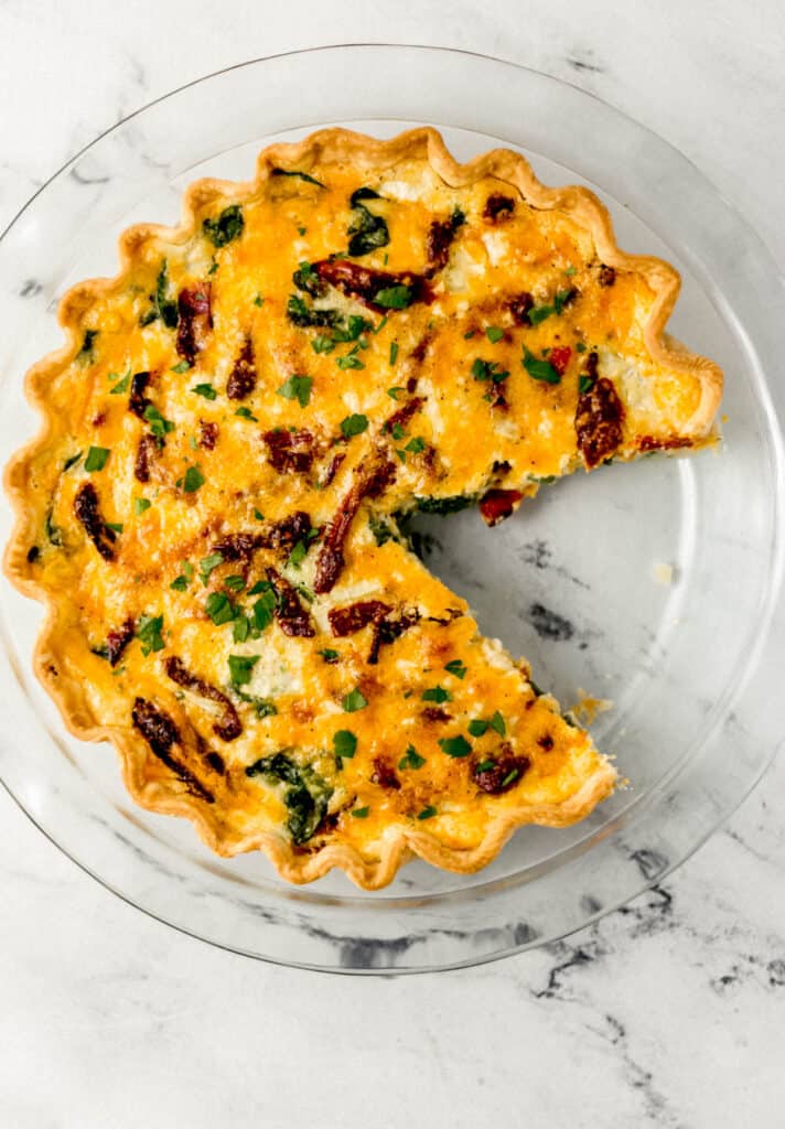 overhead view of baked quiche in a glass pie pan with a piece cut out of it