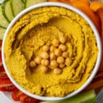 curry hummus in white bowl topped with chickpeas on top of fresh vegetables