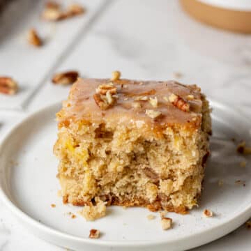 close up side view hummingbird cake on white plate topped with pecans