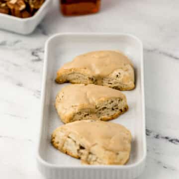 three scones on rectangle white platter with maple syrup and pecans in background