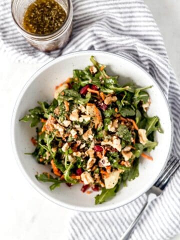 salad in white bowl beside fork on top of cloth napkin