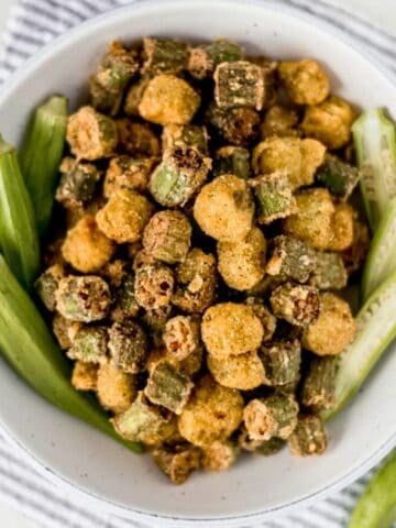 Overhead view of fresh and fried okra in a white bowl on top of a cloth napkin.