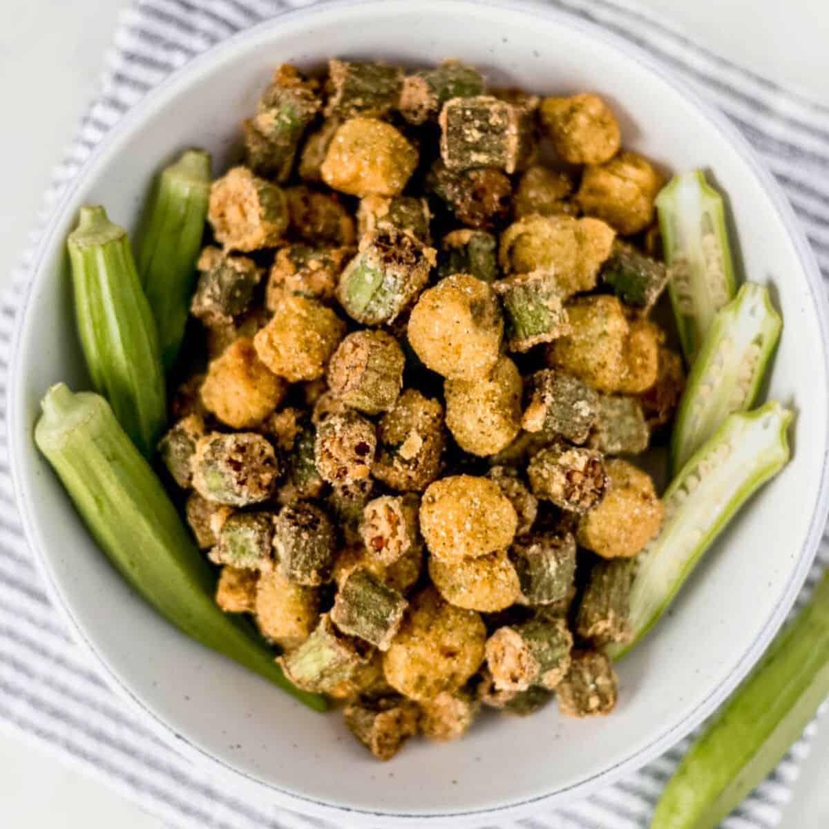 Overhead view of fresh and fried okra in a white bowl on top of a cloth napkin.