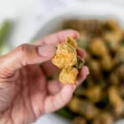 Hand holding pieces of finished okra in the air.