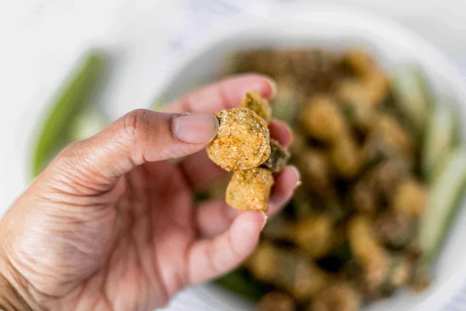 Hand holding pieces of finished okra in the air. 
