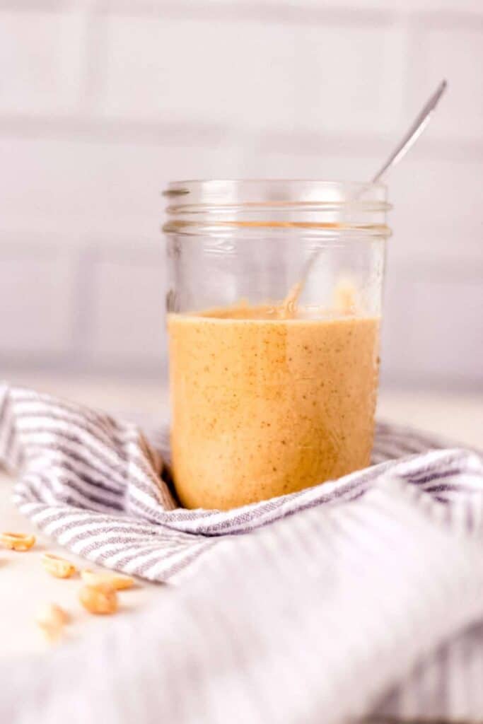 close-up side view homemade peanut butter in a jar with spoon and napkin