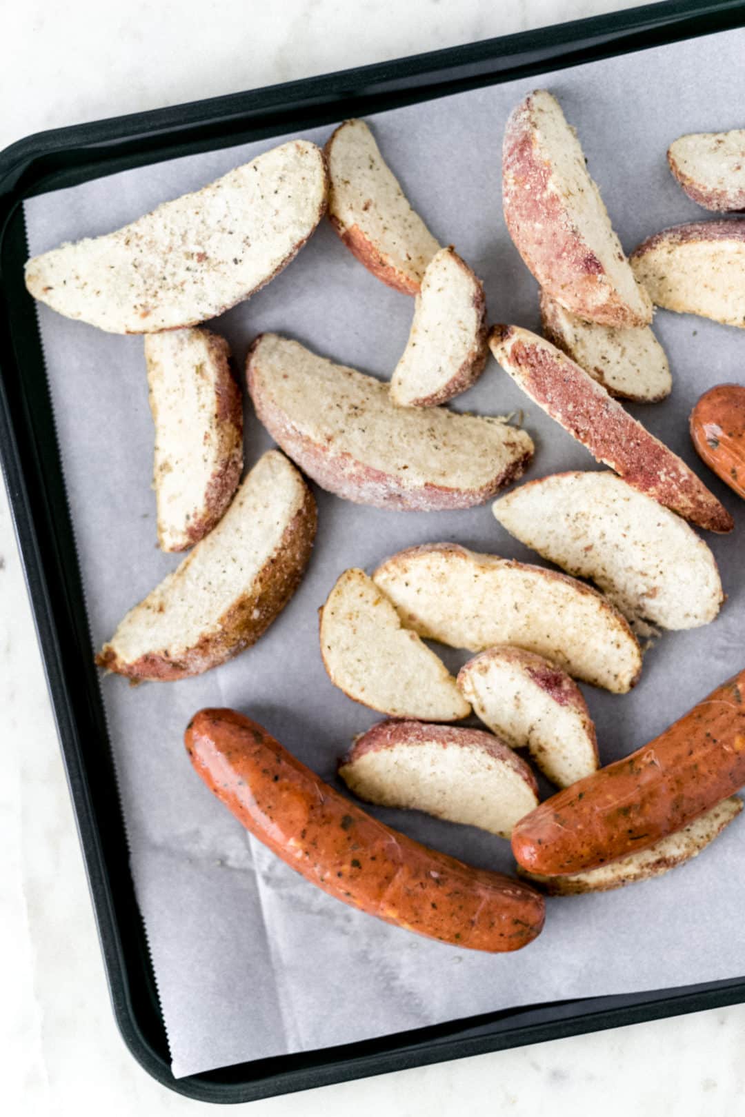 sausage and frozen potato wedges on sheet pan over parchment paper