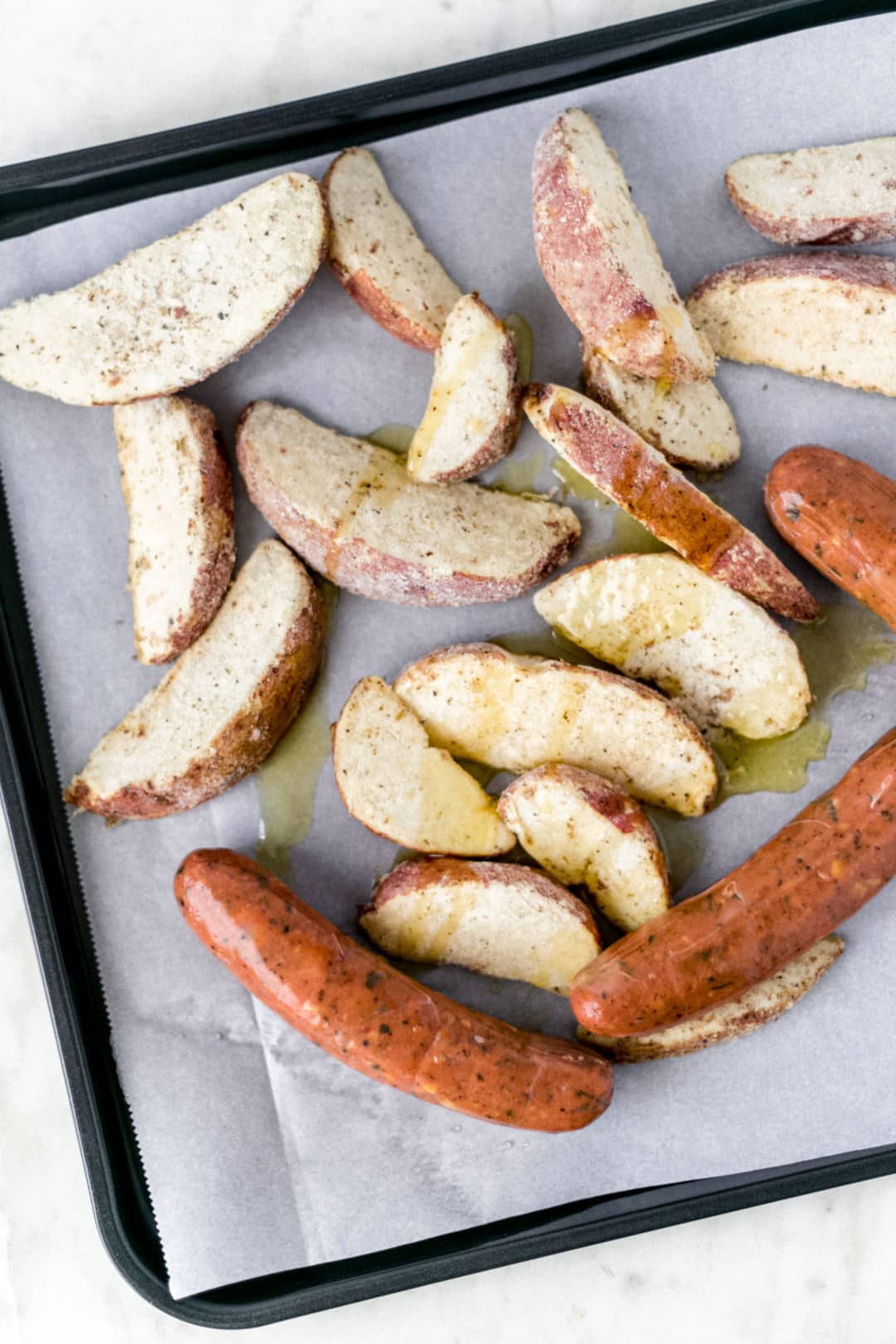 sausage, potato wedges, and olive oil on sheet pan 