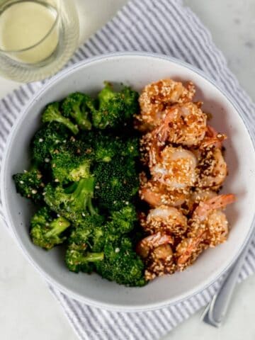 sesame shrimp in a bowl with a glass of white wine