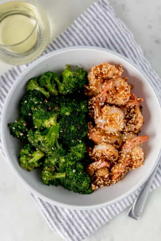overhead photo of sesame shrimp and broccoli in a bowl next to a glass of white wine