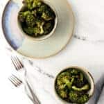 overhead shot of roasted broccoli in two small bowls on marble surface.