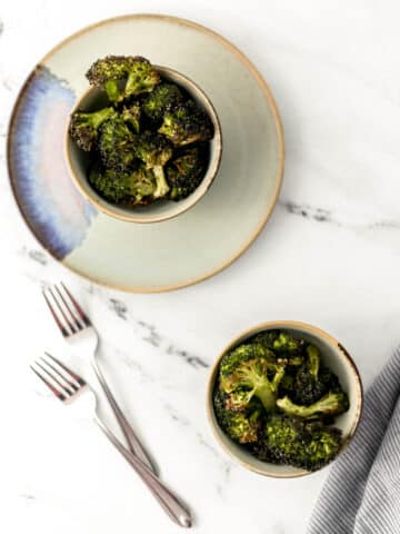 overhead shot of roasted broccoli in two small bowls on marble surface.