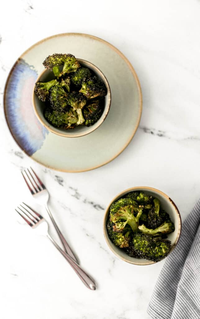 overhead shot of roasted broccoli in two small bowls on marble surface. 