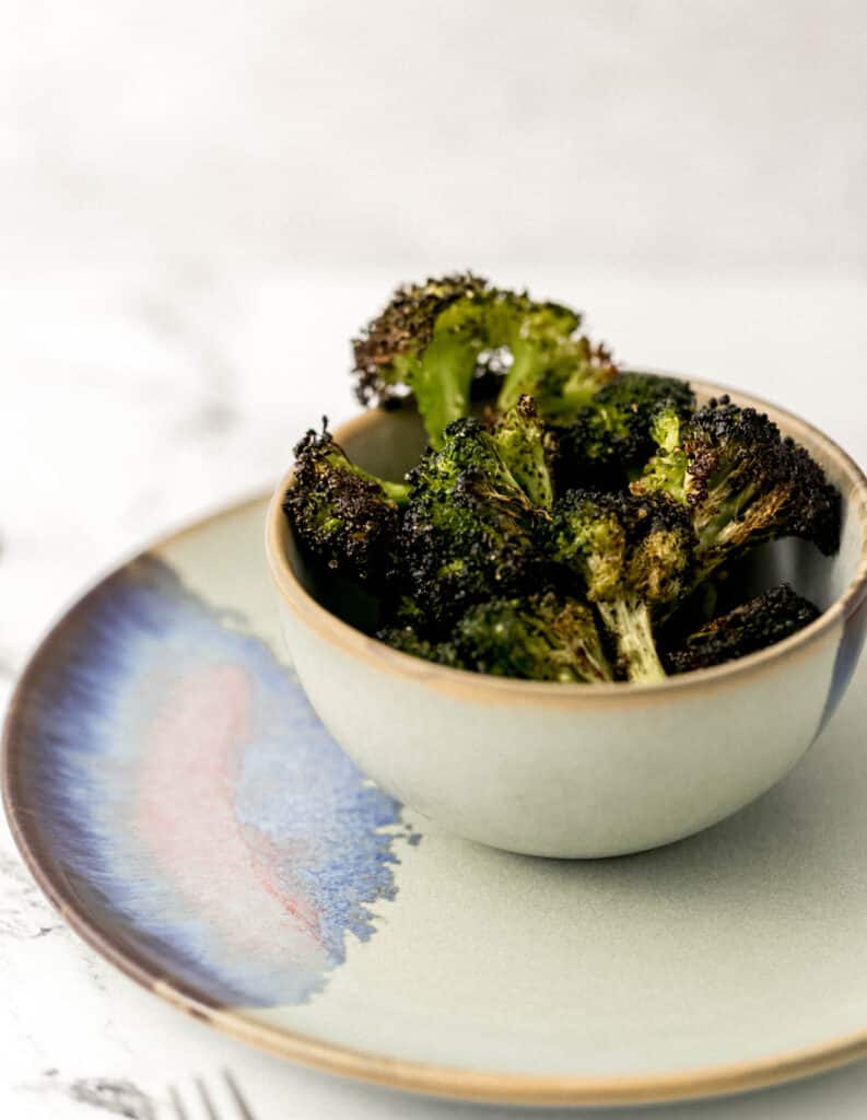 close up side view baked broccoli in small bowl over small plate. 