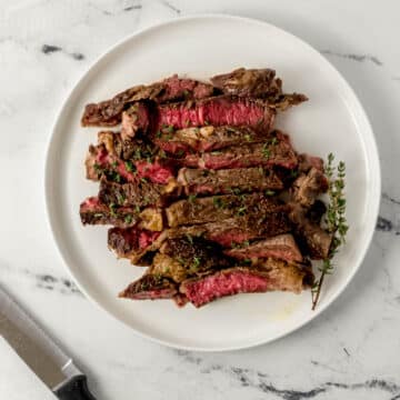 overhead view of cut steak on white plate over marble surface beside a knife