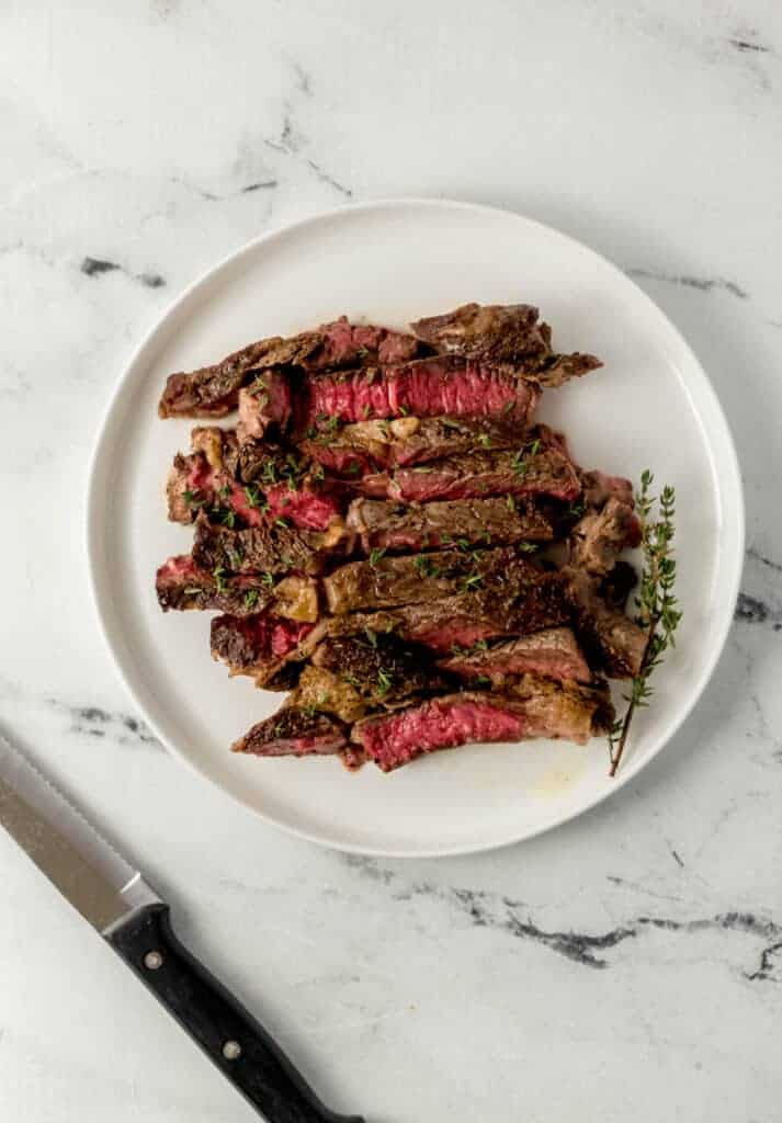 overhead view of cut steak on white plate over marble surface beside a knife