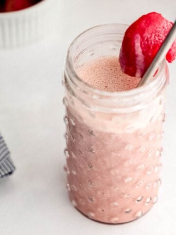 Close up side view of strawberry smoothie in glass with straw and strawberry in it.