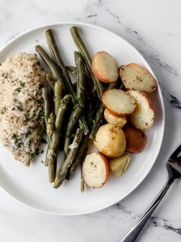 Overhead view of white plate with chicken, potatoes, and green beans beside a fork.