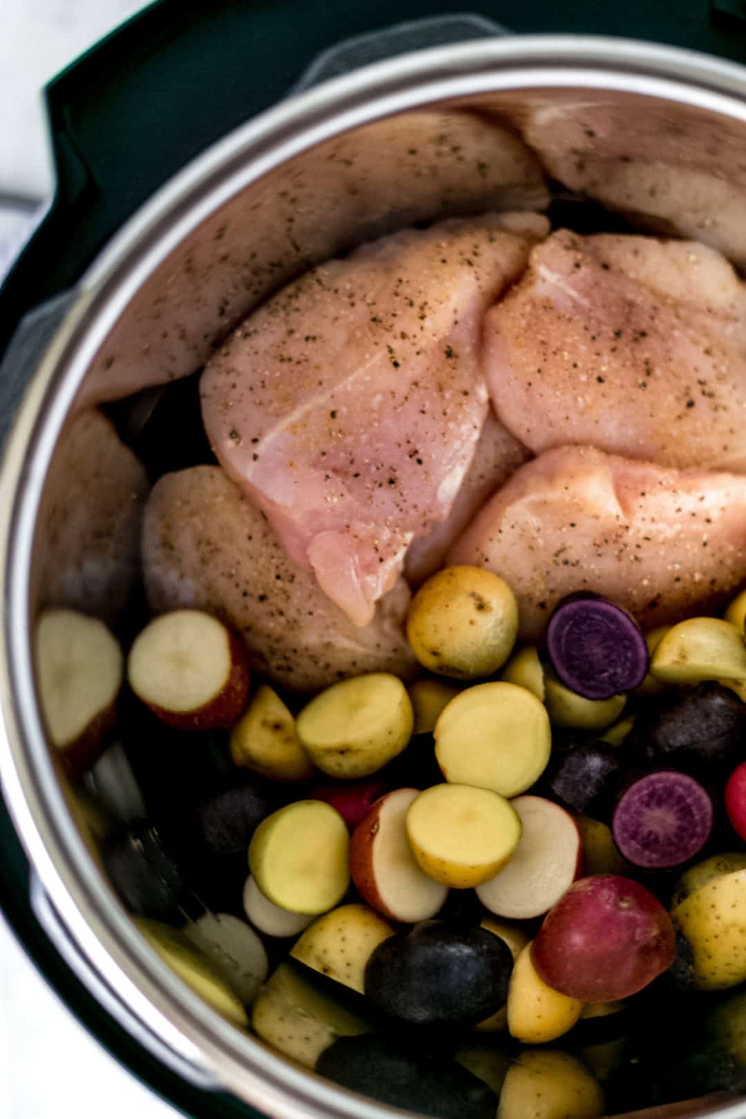 uncooked chicken and potatoes at the bottom of an instant pot