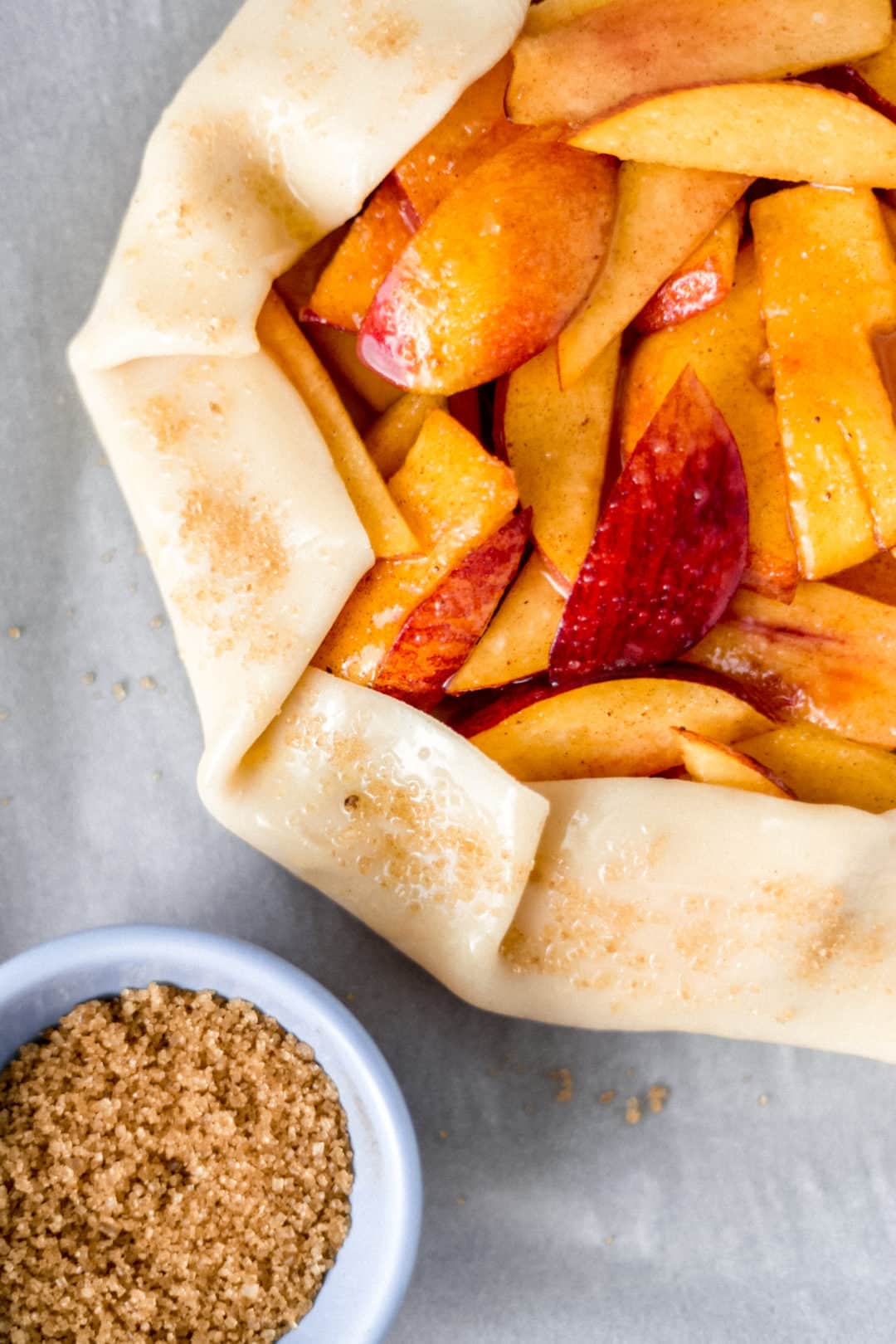 small blue bowl of raw sugar next to uncooked peach galette