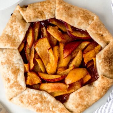 overhead view peach galette with napkin, white plates, and a knife