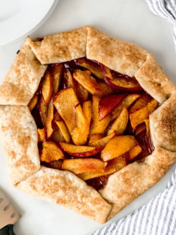 overhead view peach galette with napkin, white plates, and a knife