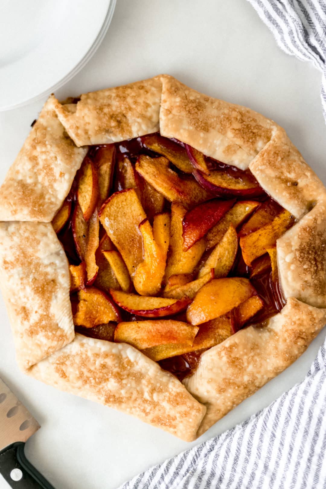 overhead view peach galette with napkin, white plates, and a knife