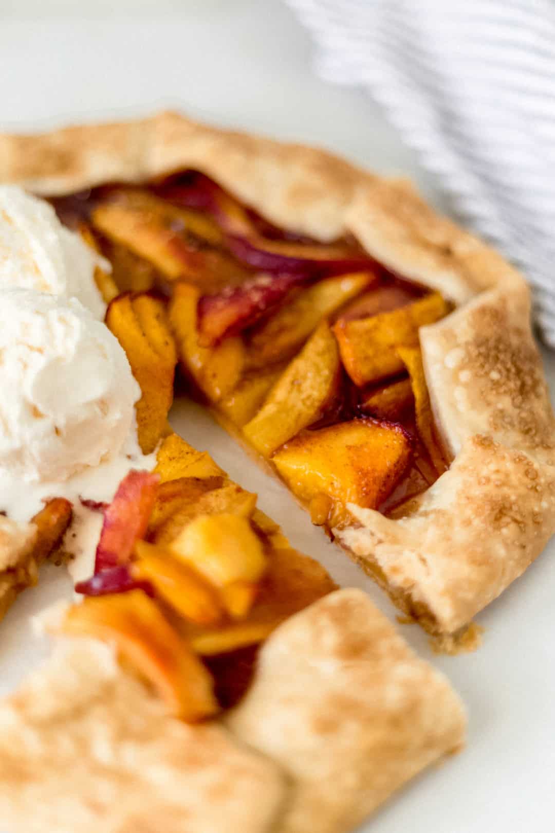 close-up side view peach galette next to a napkin and topped with vanilla ice cream