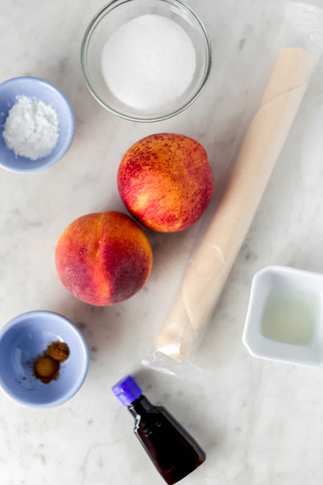 overhead view of ingredients. Two peaches, unwrapped pie crust, spices, sugar, lemon juice, cornstarch, and vanilla.