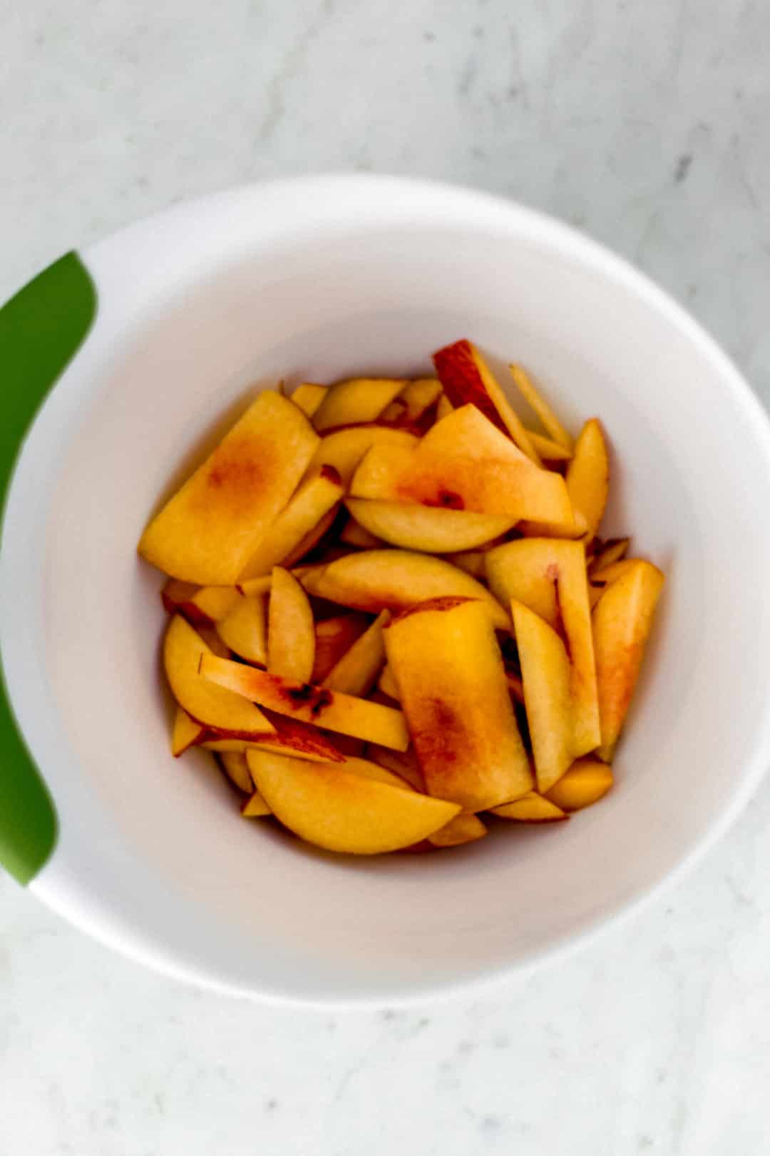 Thin slices of peaches in a large white bowl. 