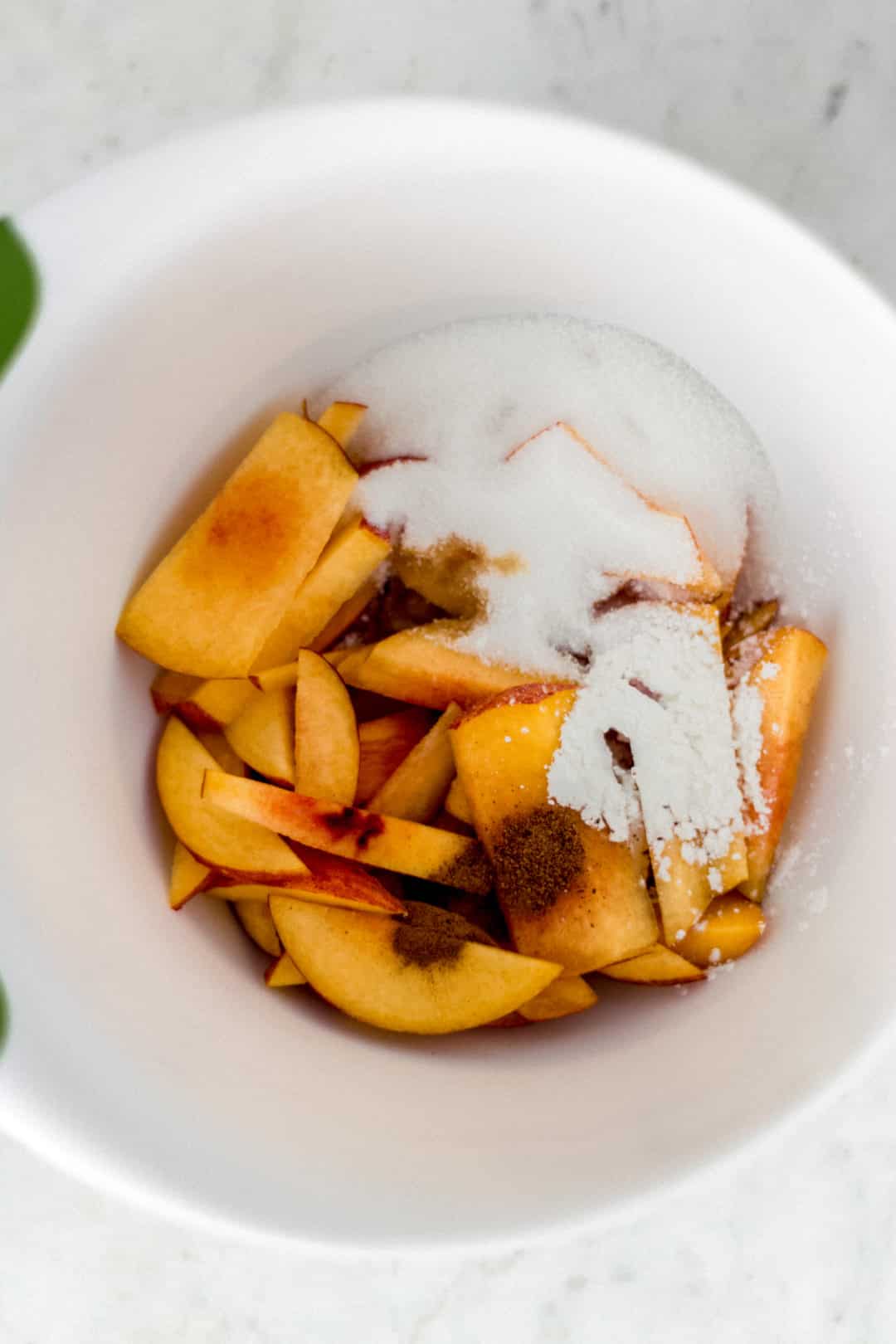 ingredients for peach galette in large white bowl with green rim