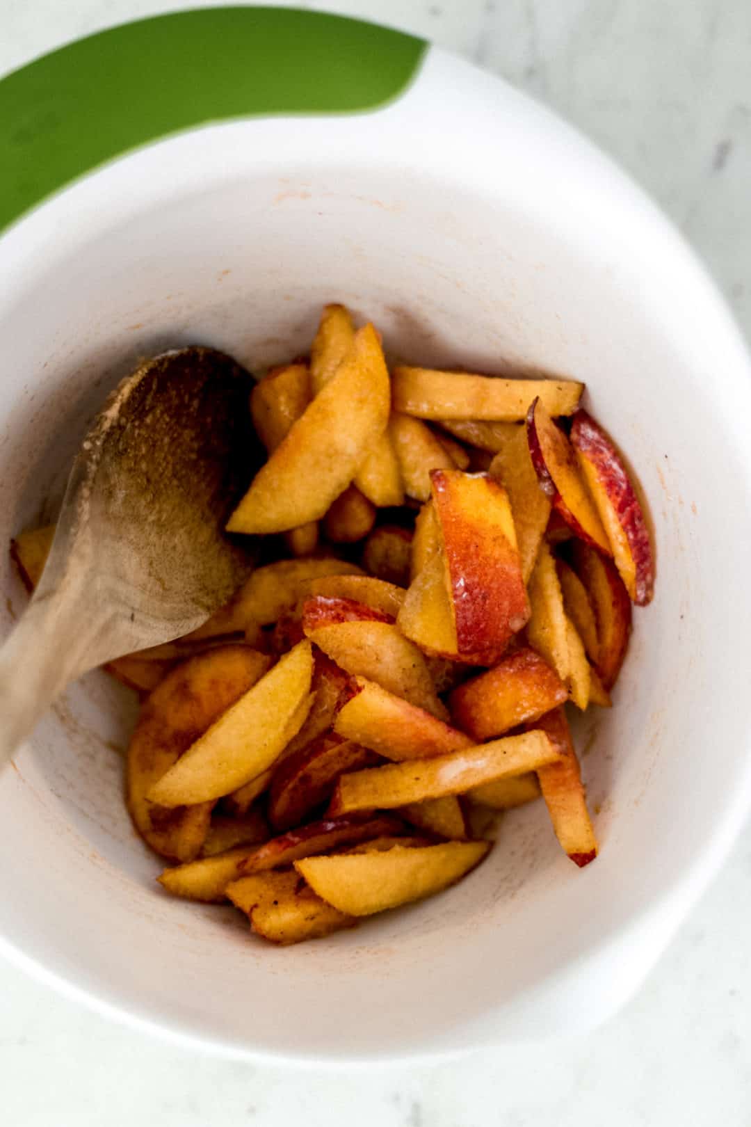 spoon in white bowl stirring sliced peaches with other ingredients