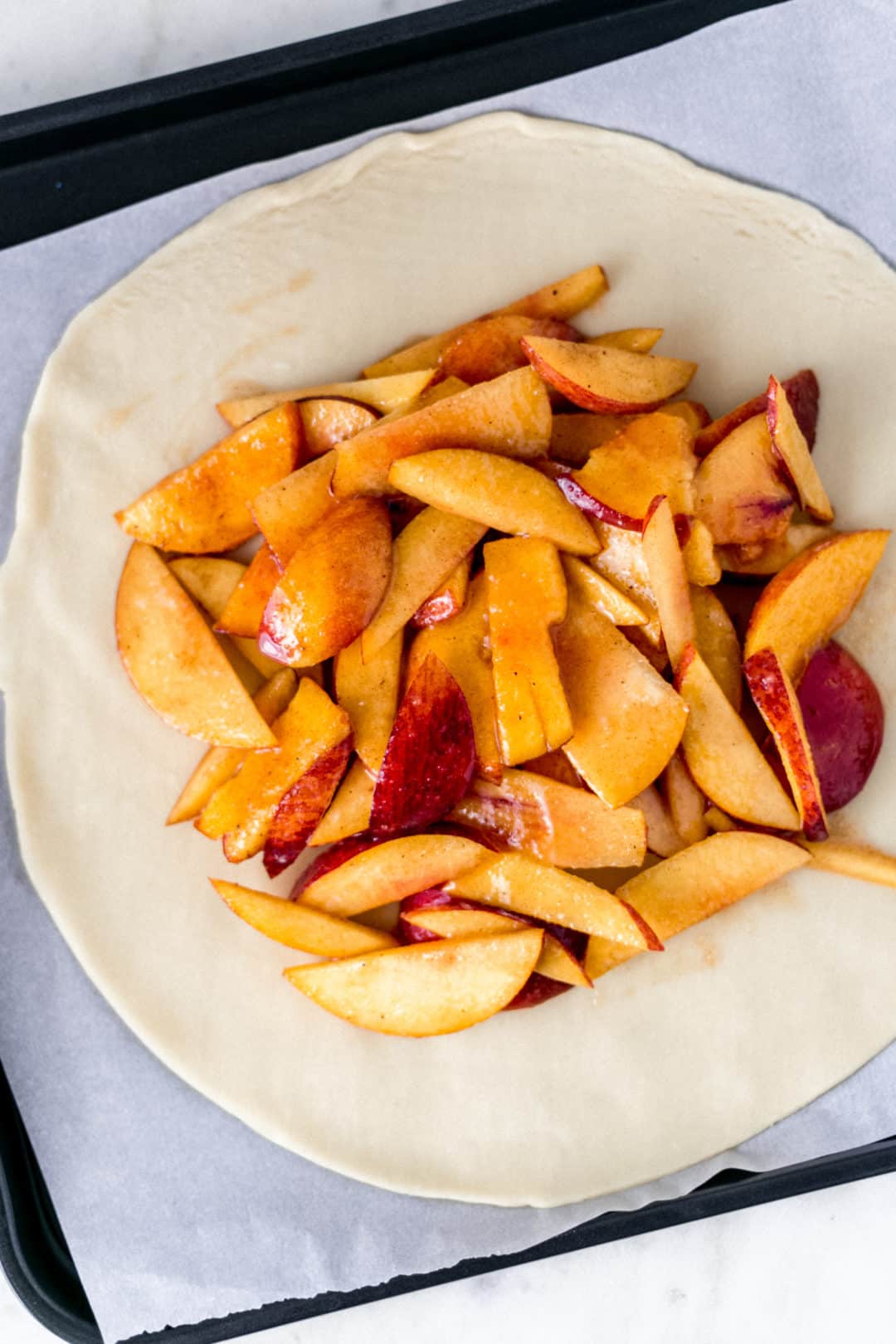 flat pie crust topped with peach mixture for peach galette