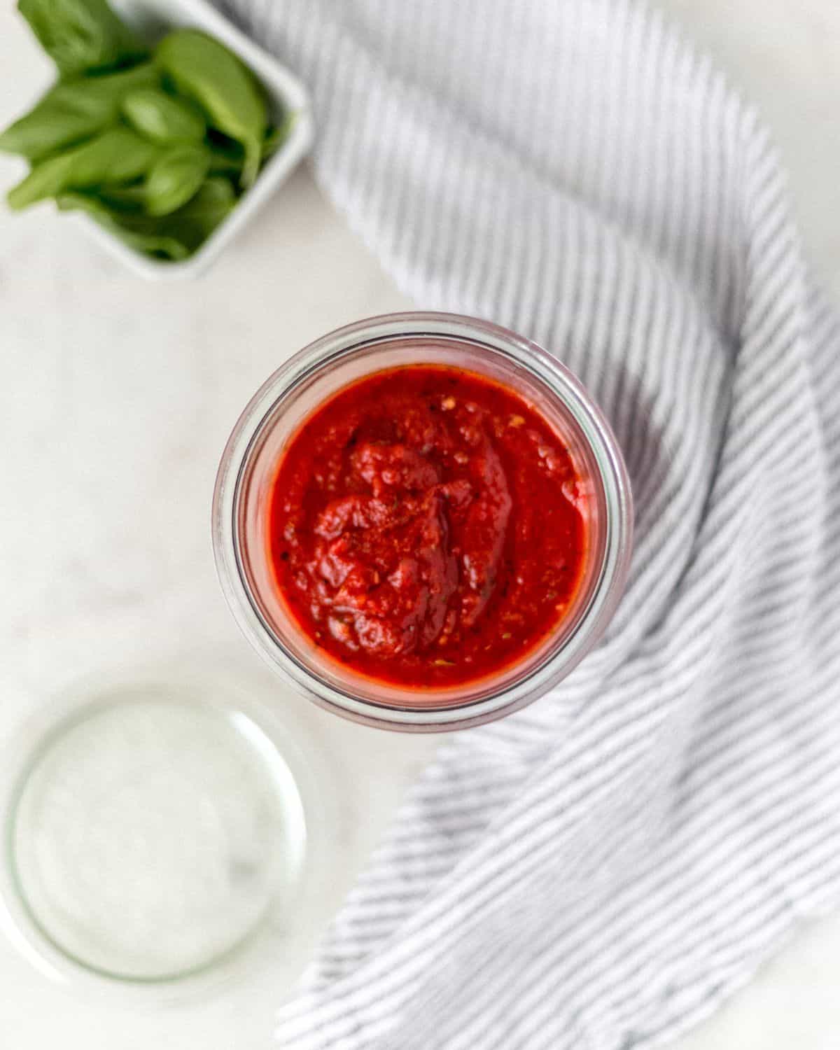 Overhead jar of sauce by lid, napkin, and bowl of basil.