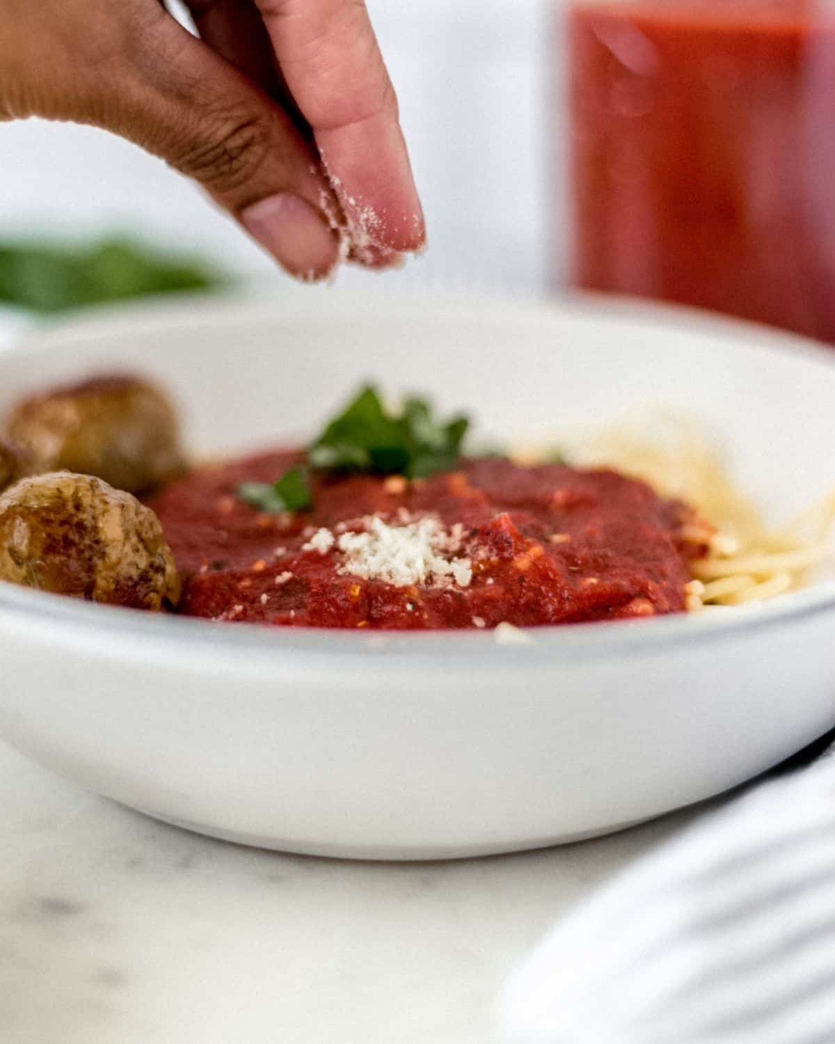 Close up side view of hand sprinkling parmesan on top of bowl of pasta.