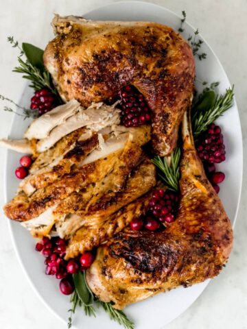 turkey arranged on white platter with fresh herbs and cranberry
