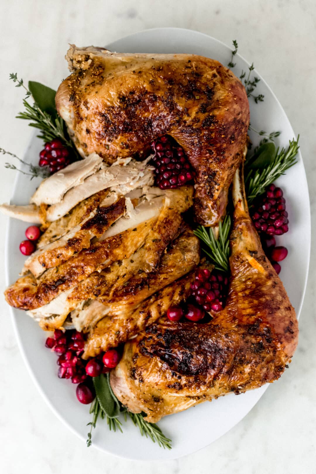 turkey arranged on white platter with fresh herbs and cranberry
