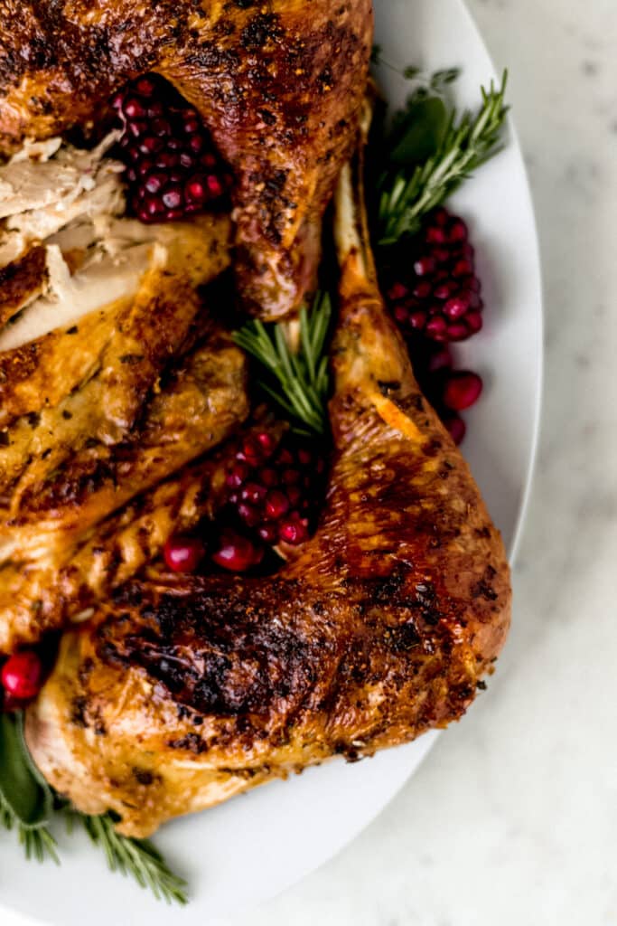 finished turkey on white platter with fresh herbs