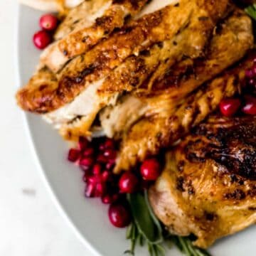 sliced turkey on large white serving platter with herbs and cranberries on it