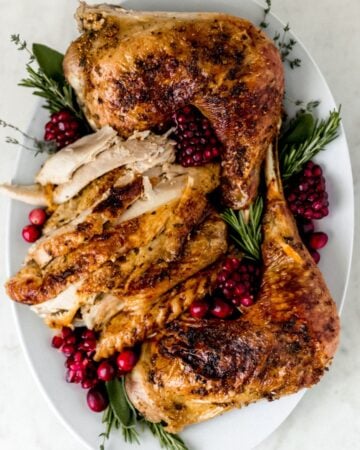 Overhead view of finished and carved turkey on white platter with garnish.