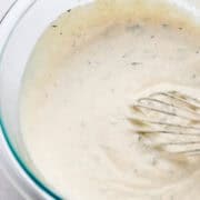 Close up view of dressing in glass bowl with whisk.