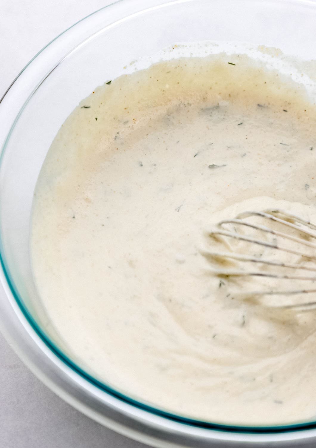 Close up view of dressing combined in glass mixing bowl with whisk. 